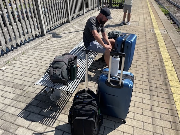 John waiting at a translation with 2 suitcases and 4 backpacks